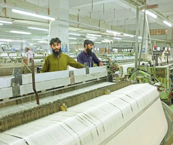 workers inspect loom machines weaving fabric at a textiles manufacturer in karachi photo reuters